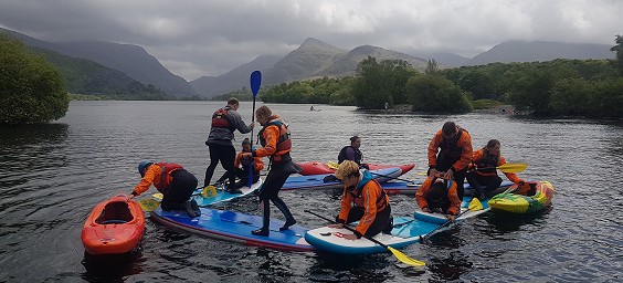 Students on a Paddlesport Instructor Award course playing a game on paddleboards and kayaks arranged in a circle